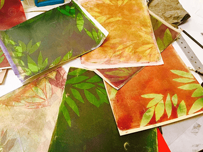 Pile of colorful papers that have been gelli printed, but have not been cut for a collage illustration yet.